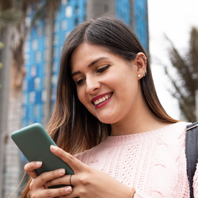 Gender-Data-Use-Impact-Advocacy-Brief-Back-Cover Smiling woman looks down at her phone against a backdrop of tall city buildings and palm trees.