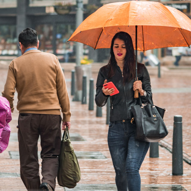 Woman looking at her phone under large umbrella in the rain on a brick walkway in Bogota, Colombia.