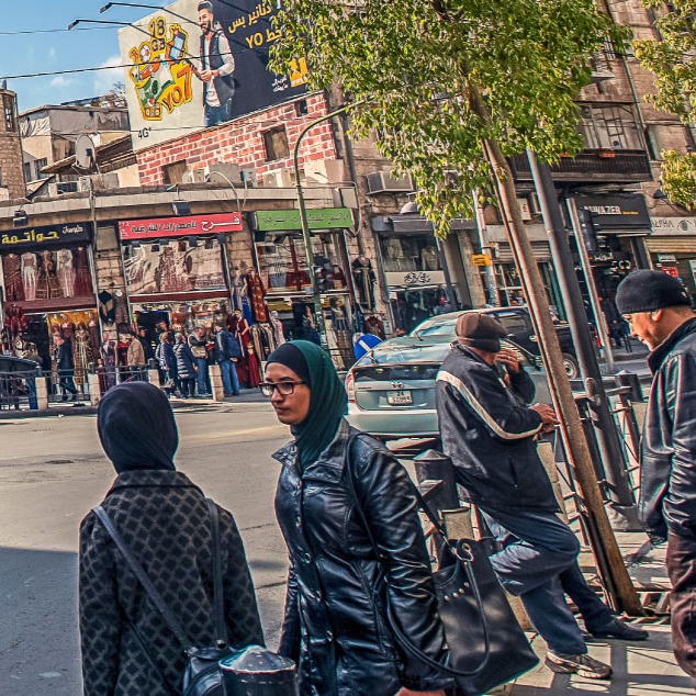 Women and men standing on the sidewalk of a busy street in Amman Jordan.
